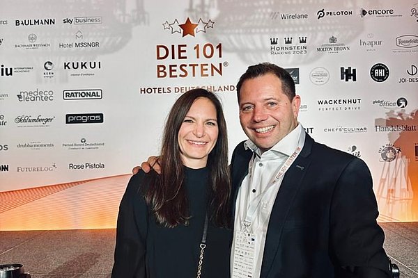Zwei Personen bei der Preisverleihung „Die 101 besten Hotels Deutschlands“ vor einer Sponsorenwand